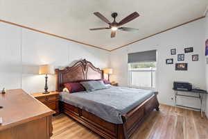 Primary bedroom featuring ornamental molding, light wood-style flooring, a textured ceiling, ceiling fan, and lofted ceiling