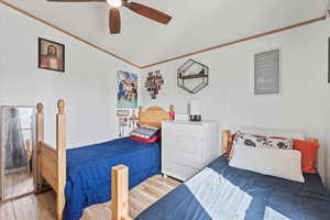 Second bedroom with ornamental molding, wood finished floors, vaulted ceiling, and ceiling fan