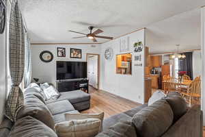 Living area with light wood-style floors, crown molding, a textured ceiling, a ceiling fan, and a chandelier