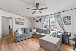 Living area with ornamental molding, a textured ceiling, light wood-style floors, vaulted ceiling, and a ceiling fan