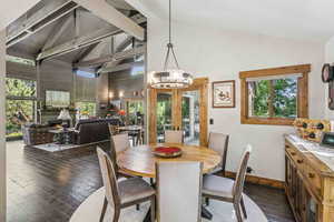 Dining room with a warm lit fireplace, high vaulted ceiling, dark wood-style flooring, french doors, and a chandelier
