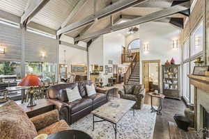 Living room featuring high vaulted ceiling, beamed ceiling, stairway, a fireplace, and dark wood finished floors