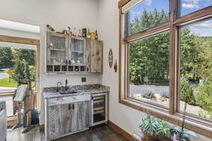 Indoor wet bar featuring dark stone counters, healthy amount of natural light, glass insert cabinets, and wine cooler