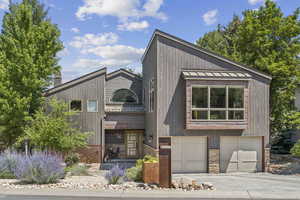 View of front of property featuring stone siding, a standing seam roof, an attached garage, driveway, and a metal roof