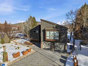View of snowy exterior with a standing seam roof, driveway, a metal roof, and an attached garage