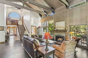 Living area featuring dark wood finished floors, high vaulted ceiling, stairway, a warm lit fireplace, and a wooden ceiling with exposed beams