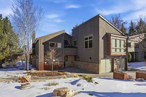 Snow covered back of property with stone siding and a garage