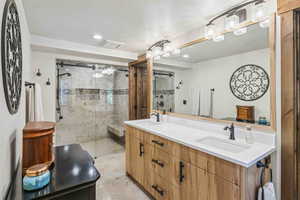 Full bathroom featuring double vanity, a shower stall, a textured ceiling, and recessed lighting