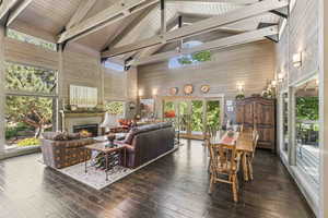 Living room with high vaulted ceiling, wood walls, a warm lit fireplace, healthy amount of natural light, and dark wood-type flooring