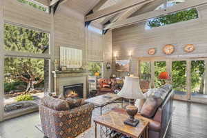 Living room featuring high vaulted ceiling, wood-type flooring, healthy amount of natural light, a large fireplace, and wood walls