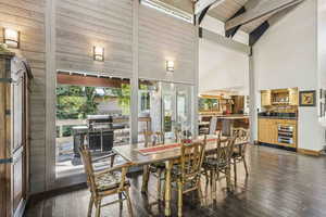 Dining space featuring beverage cooler, dark wood-style floors, high vaulted ceiling, and beamed ceiling