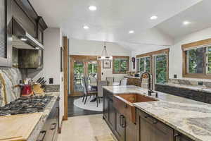 Kitchen with lofted ceiling, light stone counters, decorative light fixtures, range hood, and recessed lighting