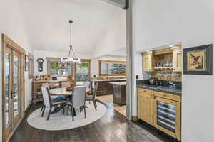 Dining room with high vaulted ceiling, wine cooler, a chandelier, dark wood-style flooring, and wet bar