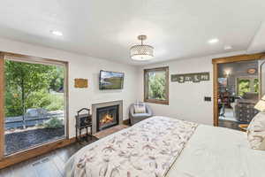 Bedroom with dark wood-style floors, a glass covered fireplace, recessed lighting, and a textured ceiling