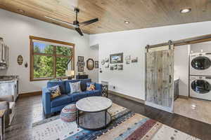 Living room with a barn door, hardwood / wood-style floors, wooden ceiling, recessed lighting, and stacked washer and clothes dryer
