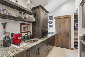 Bar area featuring dark brown cabinets, open shelves, light stone countertops, and vaulted ceiling