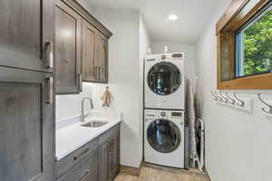 Washroom with stacked washer / drying machine, cabinet space, and light wood-style flooring