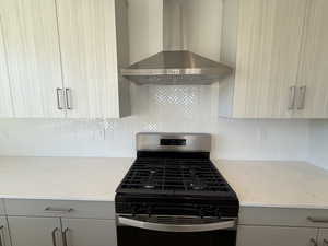 Kitchen with stainless steel gas range, wall chimney exhaust hood, light stone counters, and decorative backsplash
