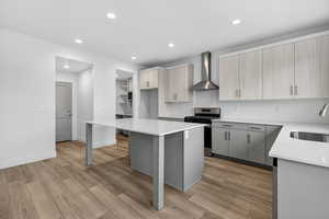 Kitchen with gray cabinets, light stone countertops, stainless steel range, wall chimney range hood, and recessed lighting