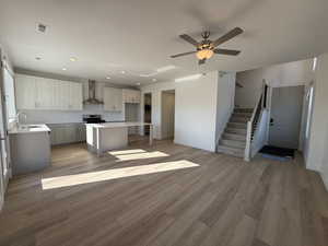Kitchen featuring gray cabinetry, wall chimney exhaust hood, light wood-style floors, recessed lighting, and open floor plan