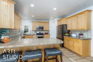 Kitchen featuring a peninsula, a breakfast bar, light brown cabinetry, stainless steel appliances, and backsplash