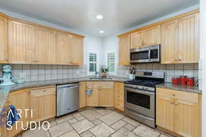 Kitchen with stainless steel appliances, light brown cabinets, light stone countertops, decorative backsplash, and recessed lighting