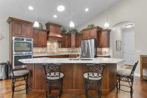 Kitchen featuring tasteful backsplash, lofted ceiling, hanging light fixtures, light stone counters, and light wood-type flooring