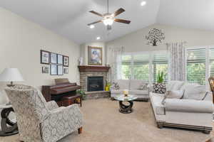 Carpeted living area with a stone fireplace, lofted ceiling, a ceiling fan, and recessed lighting