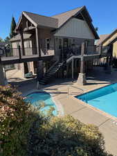 Back of house featuring stairs, a patio area, a community pool, a shingled roof, and board and batten siding