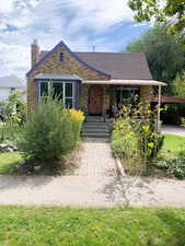 Tudor-style house with covered porch, roof with shingles, a chimney, and brick siding