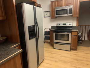 Kitchen featuring dark countertops, appliances with stainless steel finishes, brown cabinets, and light wood-style floors