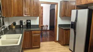 Kitchen featuring refrigerator with ice dispenser, arched walkways, dark countertops, and light wood-style flooring