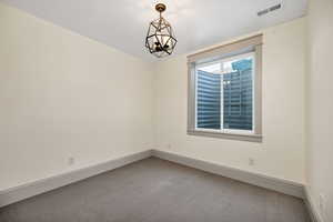 Carpeted empty room with baseboards and a chandelier