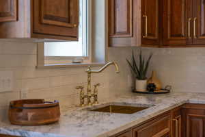 Kitchen featuring backsplash, brown cabinets, and light stone countertops
