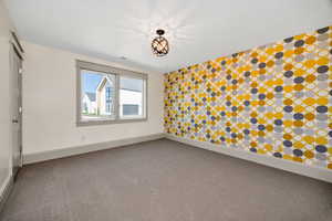 Carpeted empty room featuring wallpapered walls and an accent wall