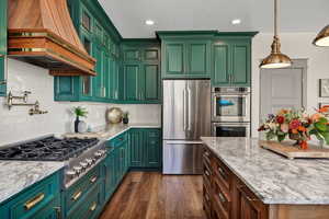Kitchen with appliances with stainless steel finishes, light stone counters, green cabinetry, dark wood-type flooring, and decorative light fixtures