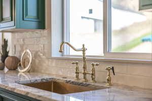 Kitchen view of backsplash, green cabinets, and light stone countertops