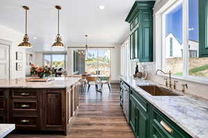 Kitchen featuring green cabinets, light stone counters, pendant lighting, dark wood finished floors, and a chandelier