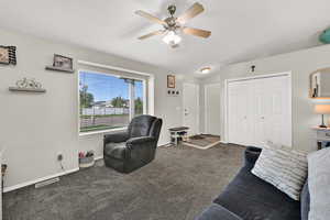 Living area featuring dark carpet, closet, and a ceiling fan