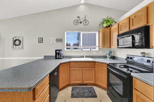 Kitchen with black appliances, a peninsula, lofted ceiling, and brown cabinets