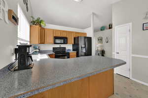 Kitchen featuring black appliances, vaulted ceiling, a peninsula, and brown cabinetry
