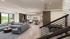 Living area featuring a raised ceiling, recessed lighting, light wood finished floors, and stairs