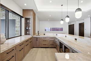 Kitchen with brown cabinetry, light stone countertops, hanging light fixtures, recessed lighting, and light wood finished floors