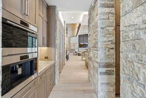 Kitchen with stainless steel double oven, light stone countertops, brown cabinets, and light wood-style floors