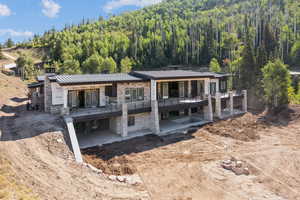 View of front of property with stone siding, a standing seam roof, a patio area, a metal roof, and a forest view