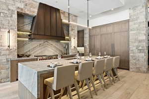 Kitchen featuring a breakfast bar, light stone counters, an island with sink, decorative light fixtures, and recessed lighting
