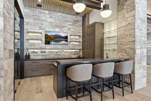 Indoor wet bar featuring dark countertops, light wood-style floors, pendant lighting, dark brown cabinets, and wooden ceiling