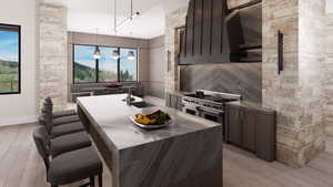 Kitchen with premium range hood, a breakfast bar area, an island with sink, light wood-type flooring, and decorative light fixtures