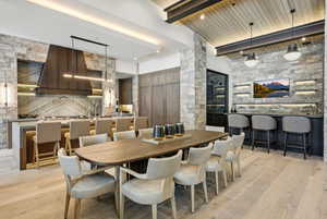 Dining area featuring a dry bar, light wood-style floors, and a wood ceiling with exposed beams
