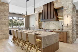 Kitchen featuring light stone countertops, a center island with sink, a kitchen breakfast bar, hanging light fixtures, and modern cabinets